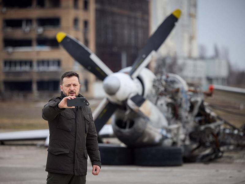 Presidente de Ucrania, Volodimir Zelenski, se toma una selfie frente a los restos del avión durante una visita en el segundo aniversario de la invasión rusa de Ucrania.