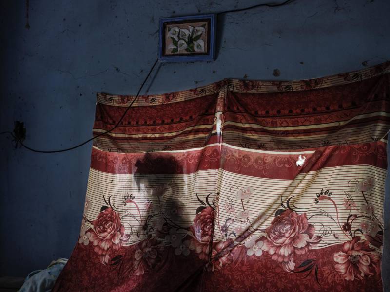 Ana, madre de seis hijos, mira por su ventana en El Guayabo, México. La pared está marcada por impactos de bala.