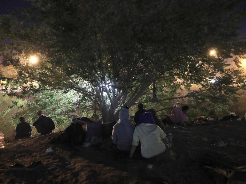 Un grupo de migrantes se protege detrás de un árbol de supuestos ataques de la Guardia Nacional de Texas.