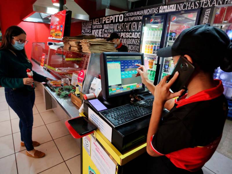 <b><span class=mln_uppercase_mln>Una cajera de un negocio de hamburguesas toma la orden de una consumidora.</span></b>