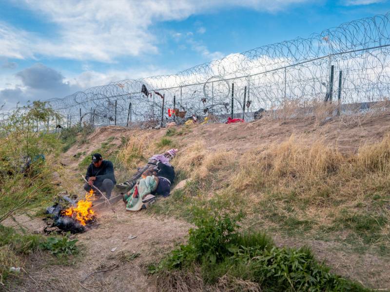 Una familia de migrantes espera frente a la cerca levantada por la Guardia Nacional de Texas para poder ingresar a EEUU.