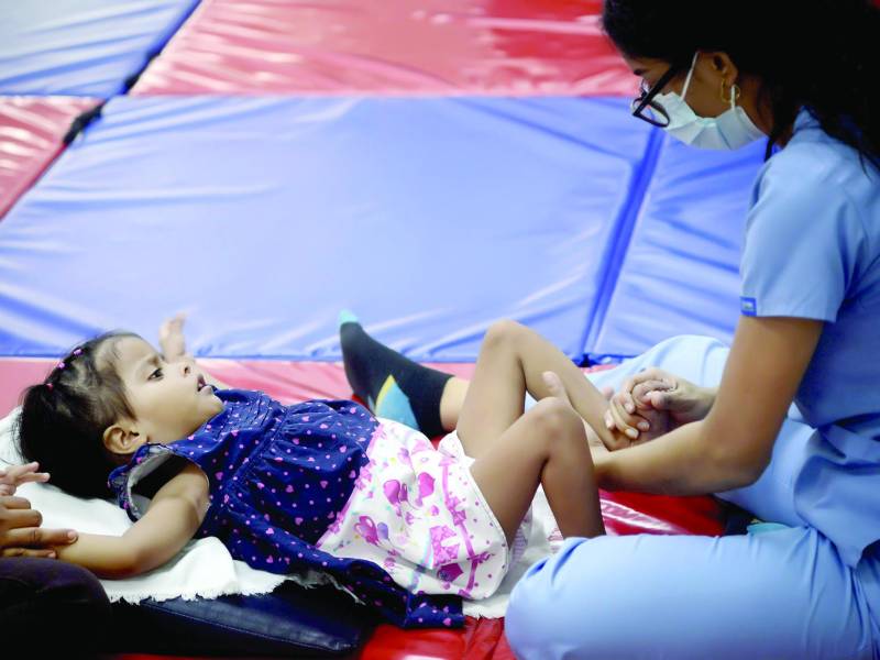 Una terapeuta practica ejercicio a una menor con discapacidad.