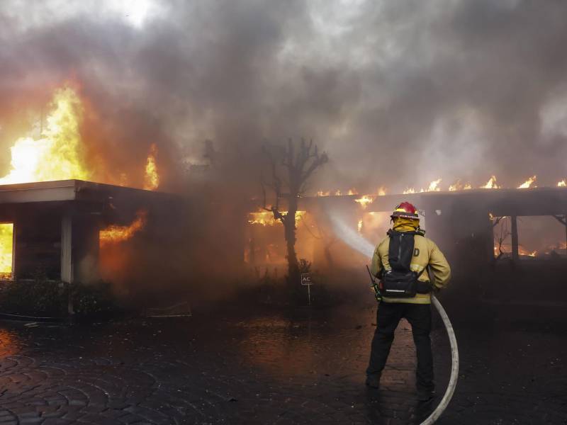 Los bomberos del condado de Los Ángeles utilizan mangueras y lanzan agua desde un helicóptero para combatir el incendio forestal de Palisades en Pacific Palisades, California, (EE.UU.). EFE/CAROLINE BREHMAN