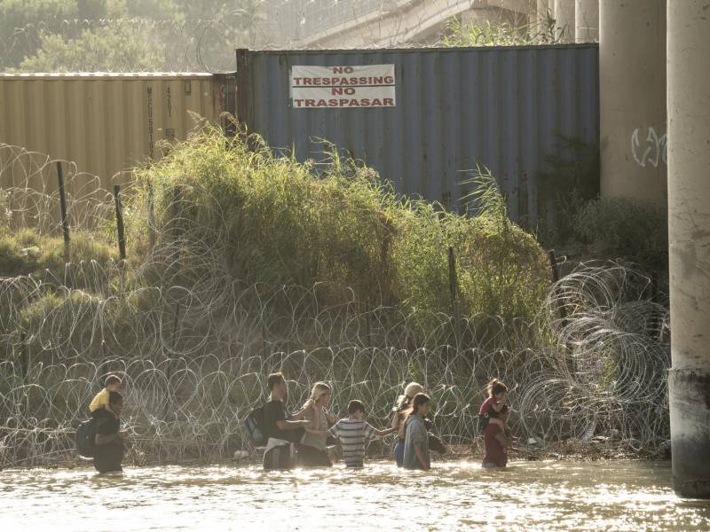 Algunos migrantes, vistos desde Piedras Negras, México, caminan a lo largo del río Bravo en busca de una abertura en la concertina en Eagle Pass, Texas, el 19 de julio de 2023.