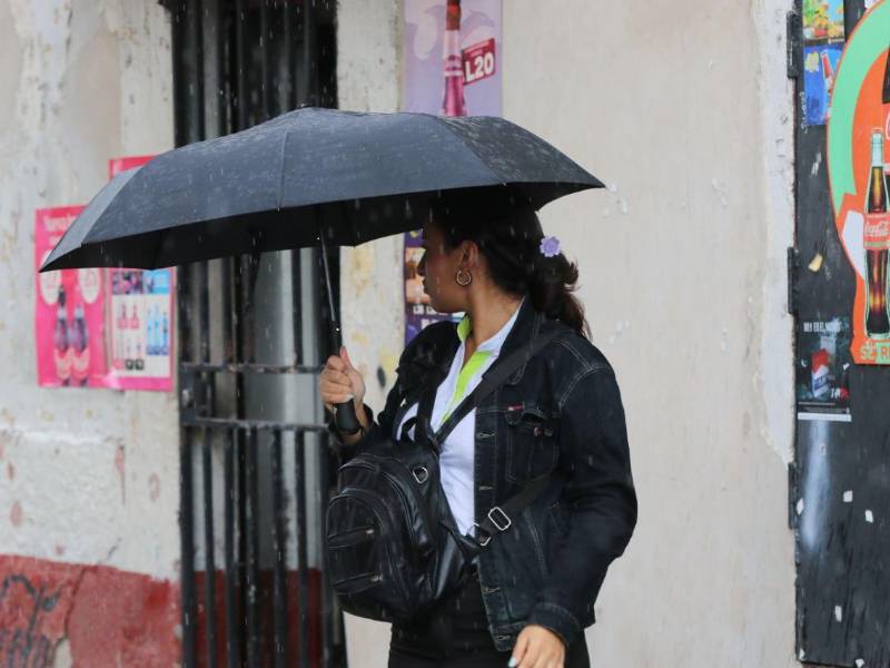 Una hondureña se protege de la lluvia en una calle de Tegucigalpa. Fotografía de archivo.