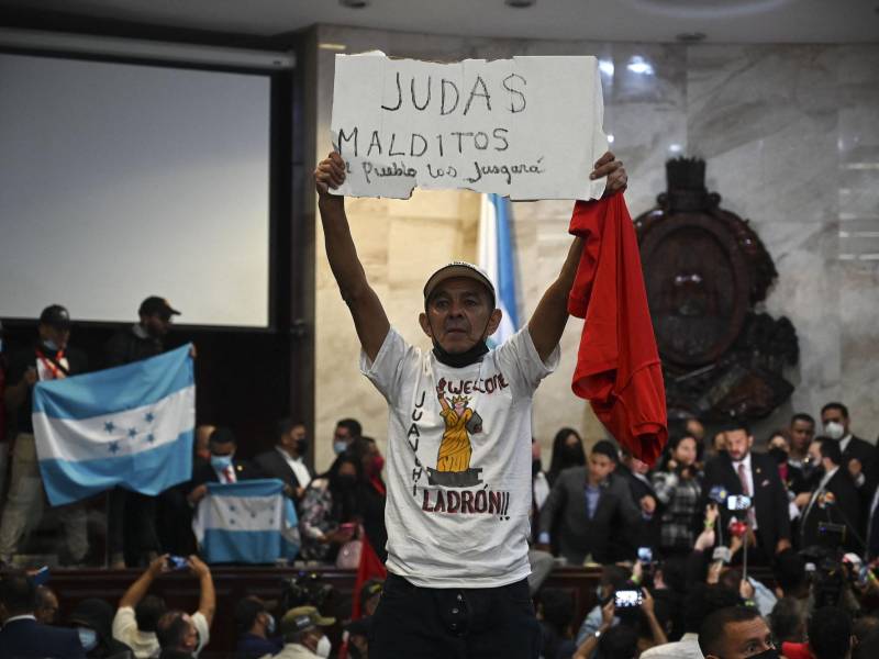 Un simpatizante del partido Libertad y Refundación (LIBRE) sostiene un cartel que dice “Maldito Judas, el pueblo te juzgará” al tomar posesión de la sede del Congreso de la República tras la elección de la Junta Directiva Provisional, en Tegucigalpa.