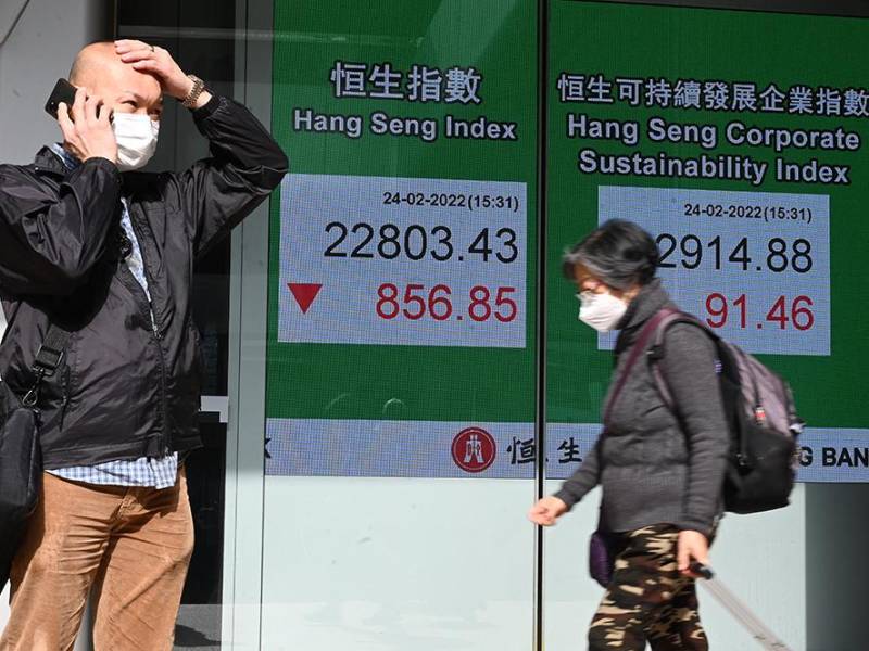 Un hombre usa su teléfono junto a un letrero que muestra los números del índice Hang Seng antes del cierre, cuando las acciones de Hong Kong cayeron el 24 de febrero de 2022 cuando se conoció la noticia de que Rusia invadió Ucrania.