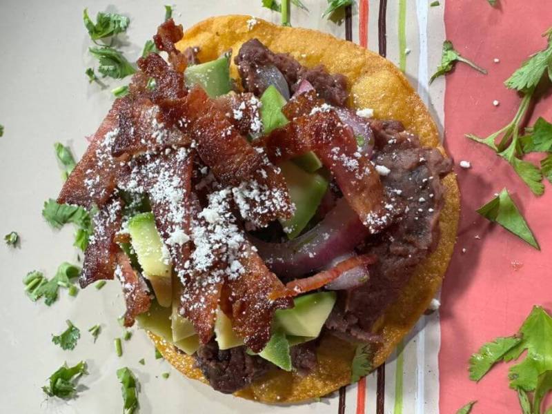 Este plato tradicional reinventado con ingredientes como tocino crujiente y cremoso aguacate, no solo expande los sabores, sino que también aporta una textura y riqueza adicionales.