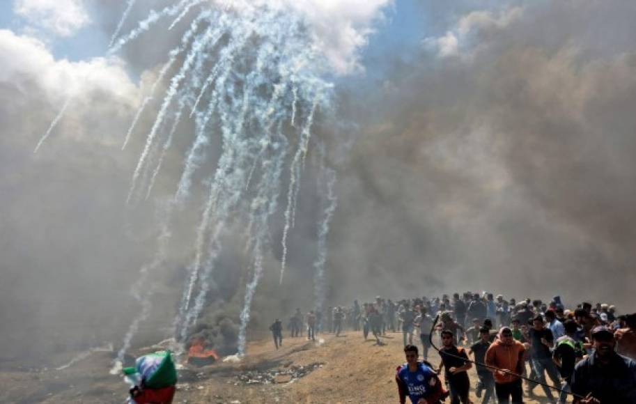 Palestinos se ponen a cubierto tras la respuesta de las fuerzas israelíes, que les arrojaron gases lacrimógenos en un intento por dispersar a los manifestantes.