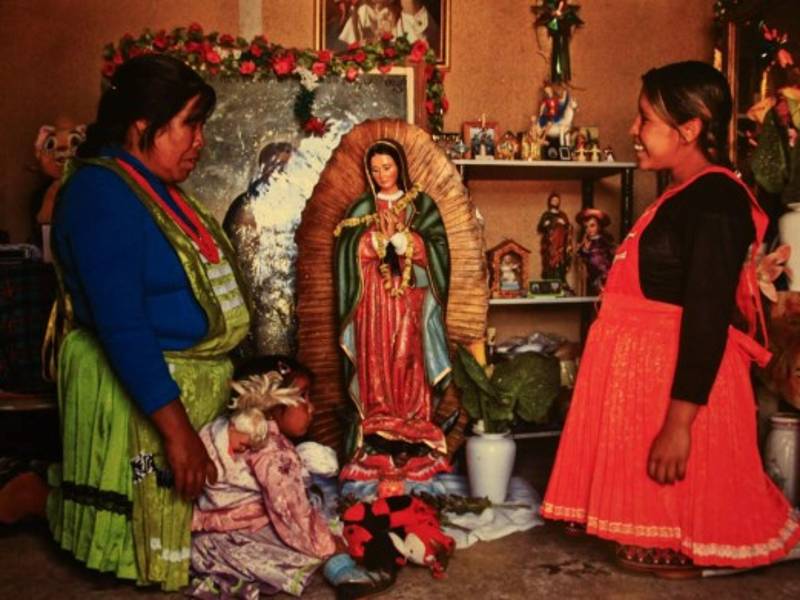 Dos mujeres indígenas frente a una imagen de la Virgen de Guadalupe. La fe es transmitida a los pequeños.