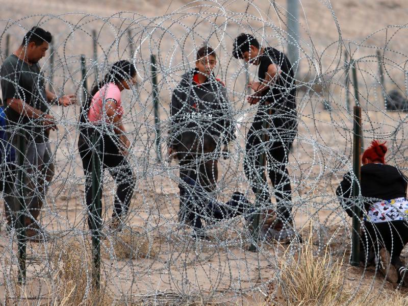 Migrantes intentan cruzar la cerca de alambres en la frontera que divide a México de los Estados Unidos.