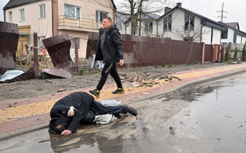 EDITORS NOTE: Graphic content / A man walks past a body of civilian in the town of Bucha, not far from the Ukrainian capital of Kyiv on April 3, 2022. - Britain, France, Germany, the US and NATO all voiced horror at Ukrainian reports on April 2, 2022, of nearly 300 bodies lying in the street in Bucha, with some appearing to have been bound by their hands and feet before being shot. (Photo by Sergei SUPINSKY / AFP)