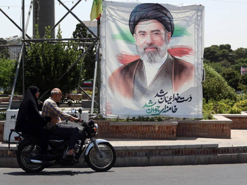 Dos personas en motocicleta cerca de una fotografía del líder supremo de Irán, Mojtaba Khamenei, en una calle de Teherán. EFE/EPA/ABEDIN TAHERKENAREH.