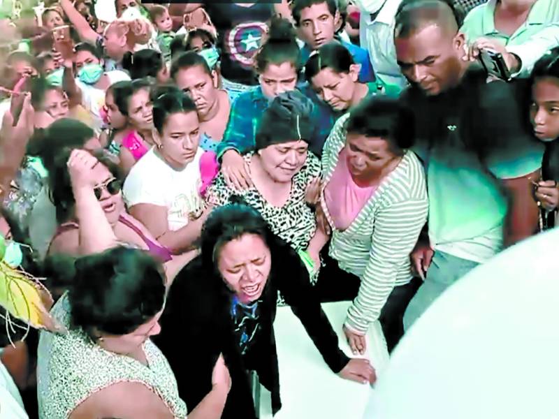 Doña Claudia Almendárez llora desconsoladamente sobre el féretro de su hijo Jeremy Janiel en el cementerio general de Guaimaca, mientras es confortada por sus familiares.