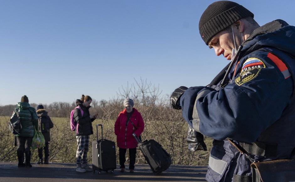 Las personas cargan sus pertenencias mientras cruzan el puesto de control fronterizo ruso mientras un rescatista del Ministerio de Emergencia ruso observa en Avilo-Uspenka.