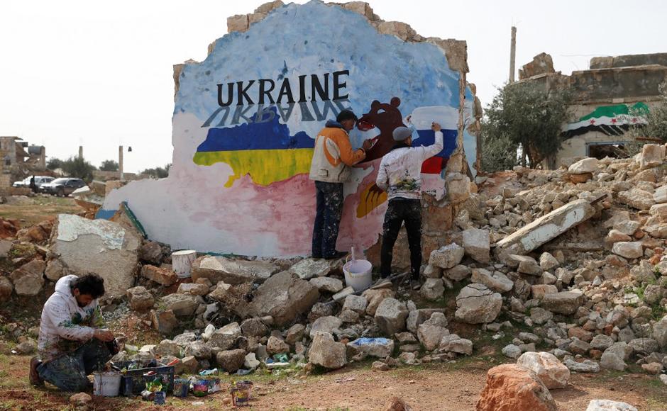 Los artistas sirios Aziz Asmar y Anis Hamdoun pintan un mural en medio de la destrucción, mostrando los colores de las banderas rusa y ucraniana, para protestar contra la operación militar de Rusia en Ucrania.