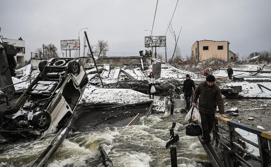 Los civiles cruzan un río en un puente volado en el frente norte de Kiev.