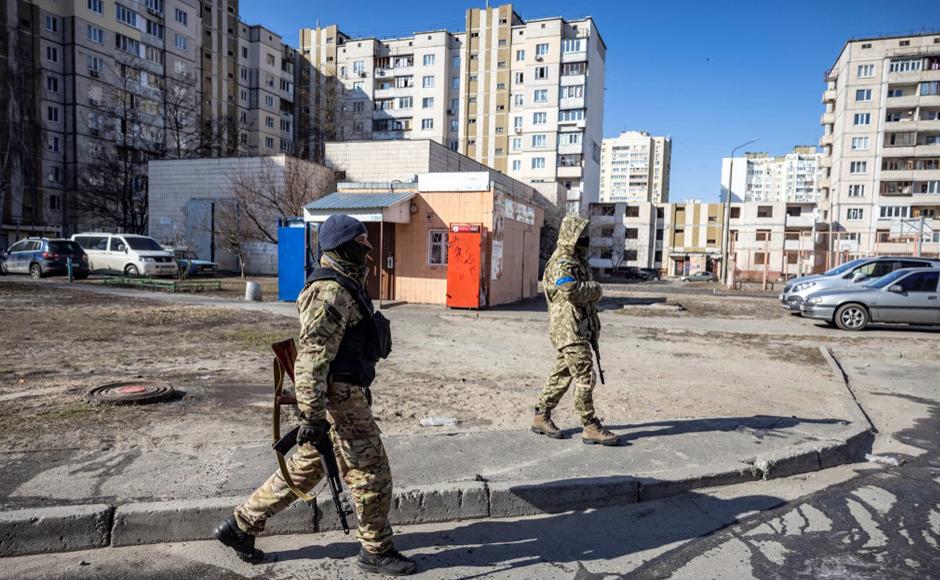 Miembros de las Fuerzas de Defensa Territorial de Ucrania caminan cerca de un edificio residencial que fue alcanzado por los escombros de un cohete.