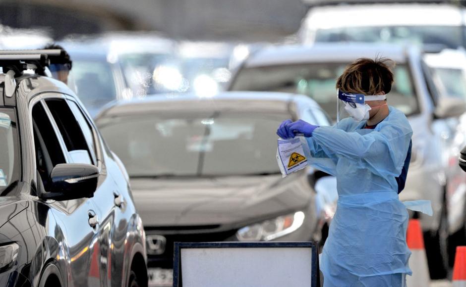 Un funcionario de Salud recolecta una prueba de covid-19 de un automovilista en un sitio de prueba en la playa de Bondi en Sydney.