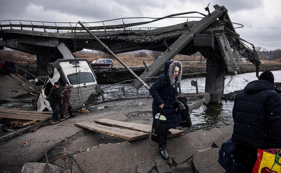 Los evacuados caminan por un camino makshift para cruzar un río junto a un puente destruido mientras huyen de la ciudad de Irpin.