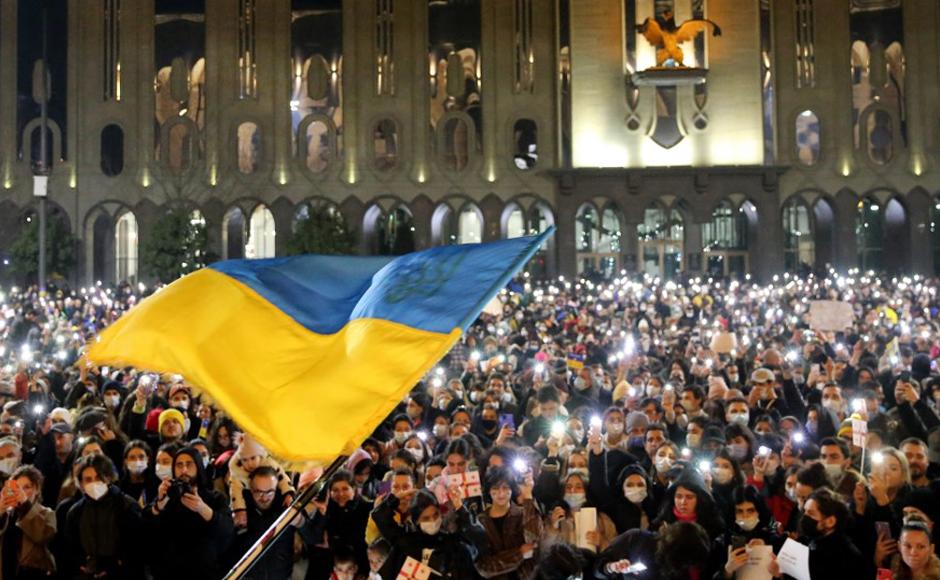 Los manifestantes sostienen sus teléfonos inteligentes con antorchas encendidas mientras se ondea una bandera ucraniana durante una manifestación en apoyo de Ucrania, en Tbilisi.