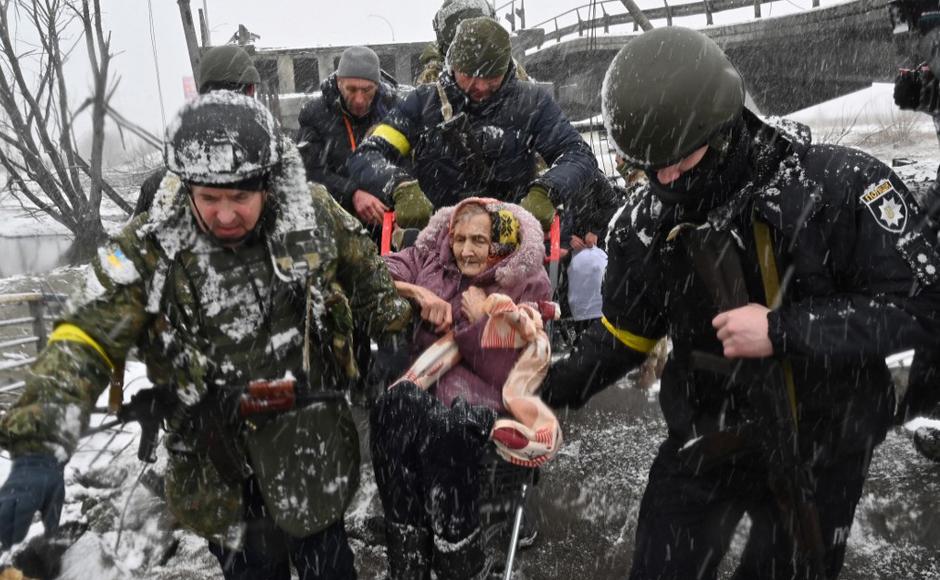 Soldados ucranianos ayudan a una anciana a cruzar un puente destruido mientras evacua la ciudad de Irpin.