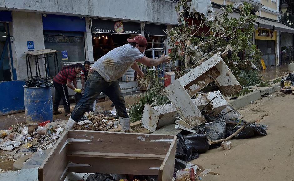 Un hombre limpia los muebles rotos frente a una tienda que fue azotada por inundaciones repentinas en Petrópolis.
