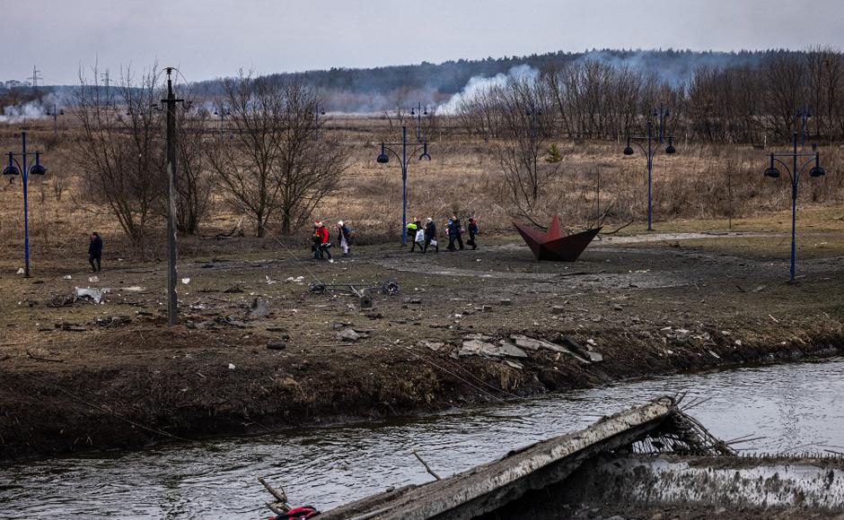 Evacuados con bolsas caminan a lo largo de la orilla del río cerca de un puente destruido mientras huyen de la ciudad de Irpin.