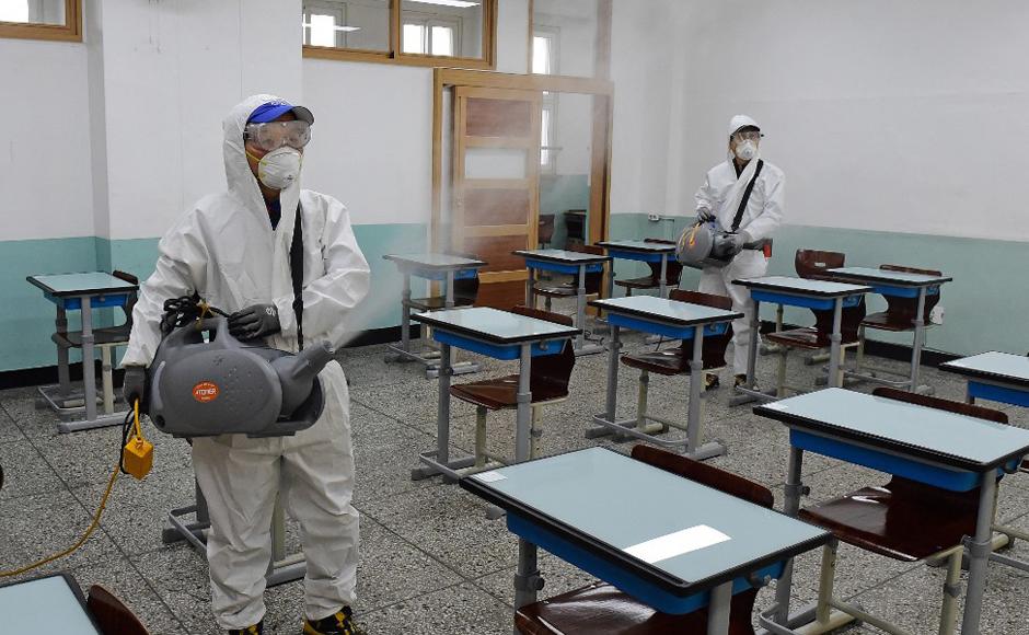 Trabajadores con equipo de protección rocían desinfectante en una sala de exámenes en una escuela secundaria en Seúl.