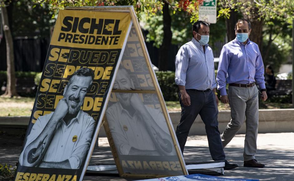 La gente pasa junto a un cartel electoral del candidato presidencial de la coalición gobernante de centro derecha, Sebastián Sichel.