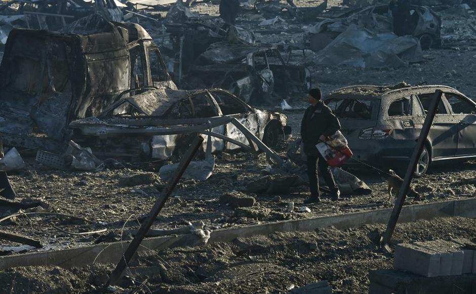Un hombre pasea a su perro entre vehículos quemados y escombros luego de un ataque con misiles.
