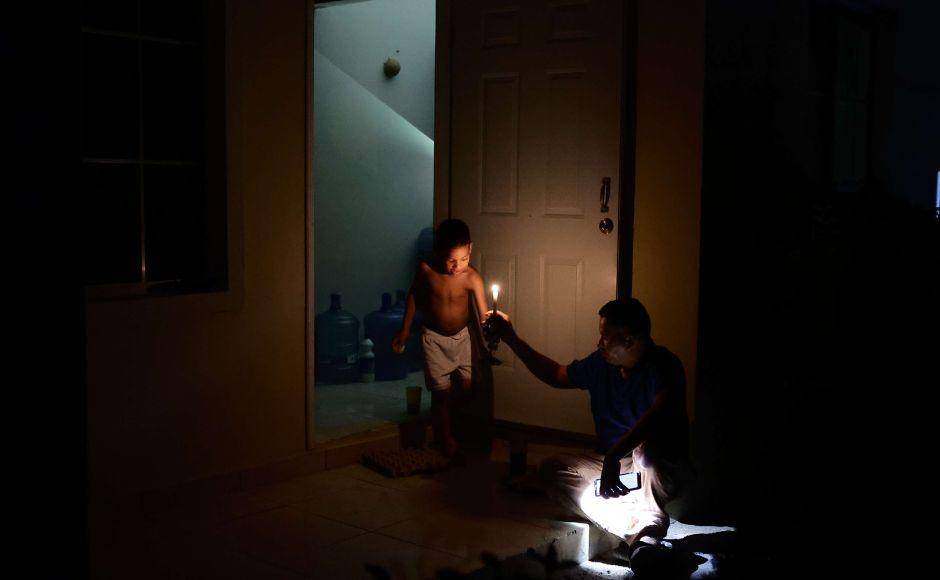 $!Un padre y su hijo permanecen en la sala de su casa, tratando de pasar la noche mientras una vela ilumina la morada.