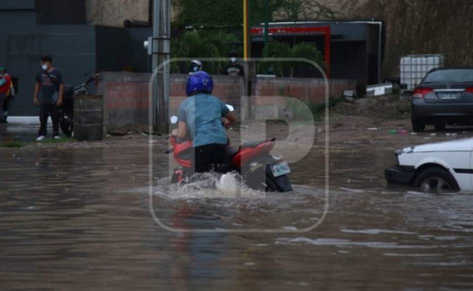Un conductor de motocicleta empuja su vehículo tras averiarse debido al agua.