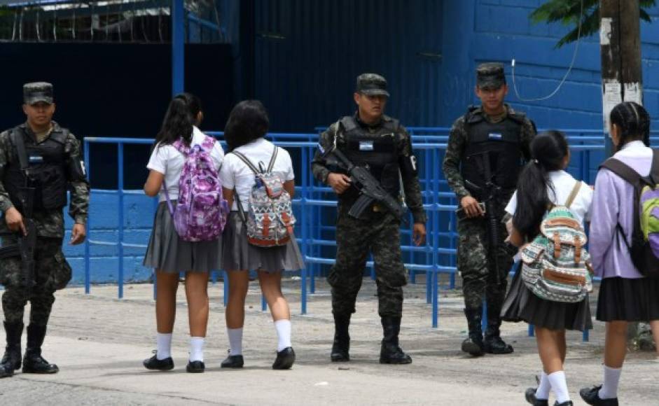 Policías militares armados vigilan la entrada y alrededores del Instituto Saúl Zelaya de la capital de Honduras, mientras otros desarmados circulan por los pasillos y conversan con los alumnos de este colegio asediado por pandillas. AFP
