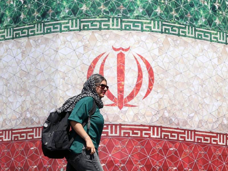 Una mujer iraní pasa junto a una valla publicitaria con la bandera nacional de Irán en la plaza Enqelab de Teherán, Irán. EFE/EPA/ABEDIN TAHERKENAREH.