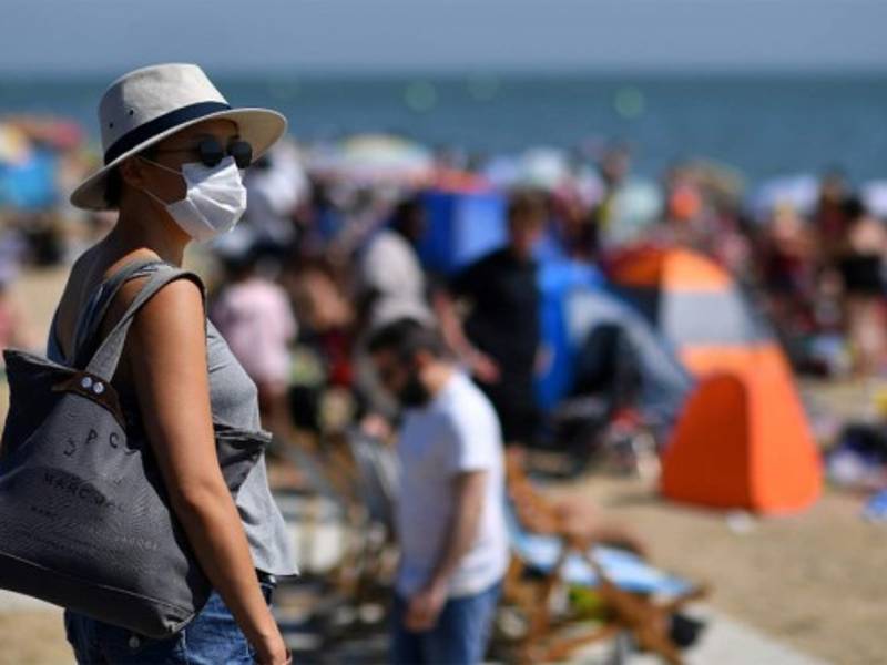 Una mujer que usa PPE una máscara facial como medida preventiva contra la propagación de COVID-19, llega a la playa en Inglaterra. Foto AFP