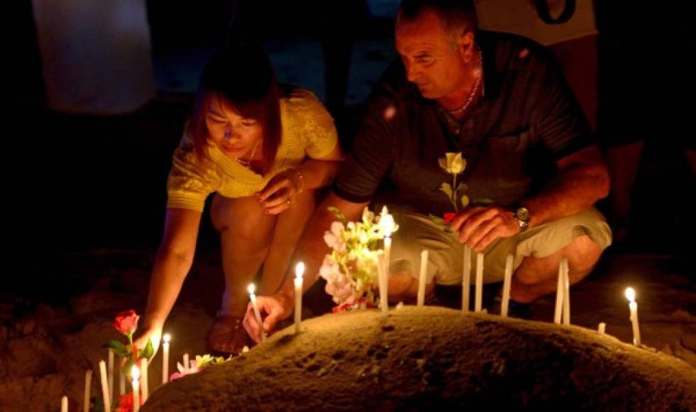 Tailandeses y turistas extranjeros colocan velas en una escultura de arena durante la conmemoración del décimo aniversario del tsunami de 2004 en la playa de Patong, en la provincia de Phuket.
