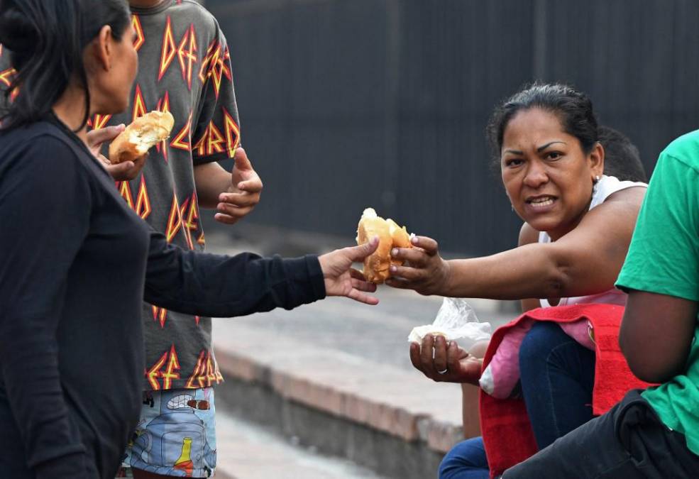  Migrantes venezolanos comparten pan mientras esperan afuera del Banco Central de Honduras.