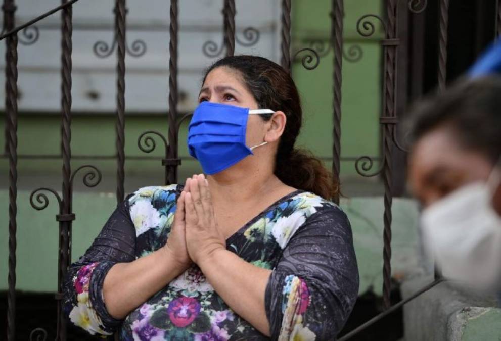 A woman prays wearing a face mask to fight the spread of the COVID-19 coronavirus, as she looks at a car procession commemorating Jesus Christ's crucifixion during Good Friday, in Tegucigalpa, on April 10, 2020. (Photo by ORLANDO SIERRA / AFP)