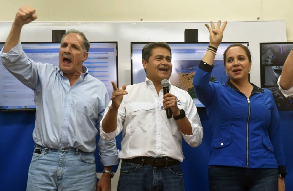 Honduran President and presidential candidate Juan Orlando Hernandez (C), his wife Ana Garcia de Hernandez (R) and Tegucigalpa Mayor Nasry Asura (L) wave to supporters in Tegucigalpa during the general elections on November 26, 2017. Honduras' six million voters are to cast ballots in a controversial election Sunday in which President Juan Orlando Hernandez is seeking a second mandate despite a constitutional one-term limit. This small country is at the heart of Central America's 'triangle of death,' an area plagued by gangs and poverty. / AFP PHOTO / RODRIGO ARANGUA