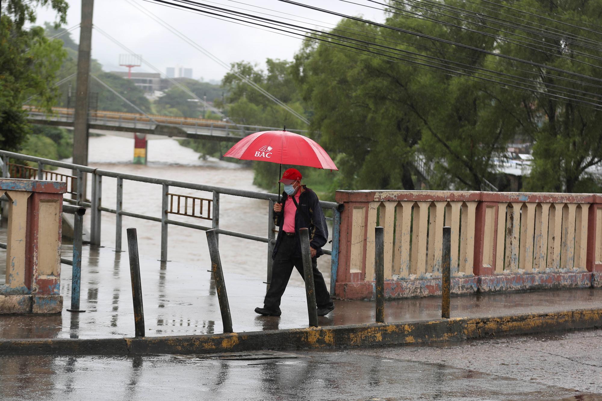 Un ciudadano camina mientras al fondo se ve el elevado nivel del río Choluteca, en Tegucigalpa (Honduras). EFE/Gustavo Amador