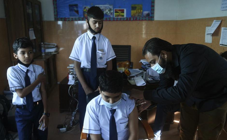 Un trabajador de la salud inocula a un estudiante con una dosis de la vacuna Pfizer contra el coronavirus en una escuela en Karachi.