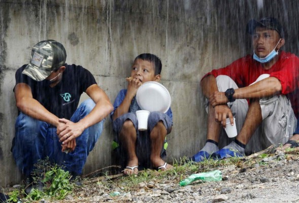 A child eats next to men as they take refuge under La Democracia bridge while waiting for relatives to be rescued by navy members from floods caused by the passage of Hurricane Iota in El Progreso, Yoro department, Honduras, on November 19, 2020. - Iota's death toll rose to 38 on Wednesday after the year's biggest Atlantic storm unleashed mudslides, tore apart buildings and left thousands homeless across Central America, revisiting areas devastated by another hurricane just two weeks ago. (Photo by STR / AFP)