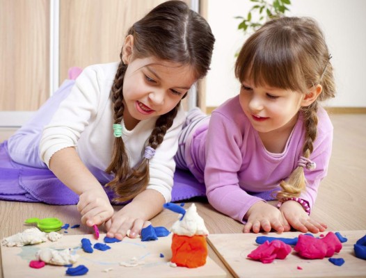Two little girls are playing with plasticine.