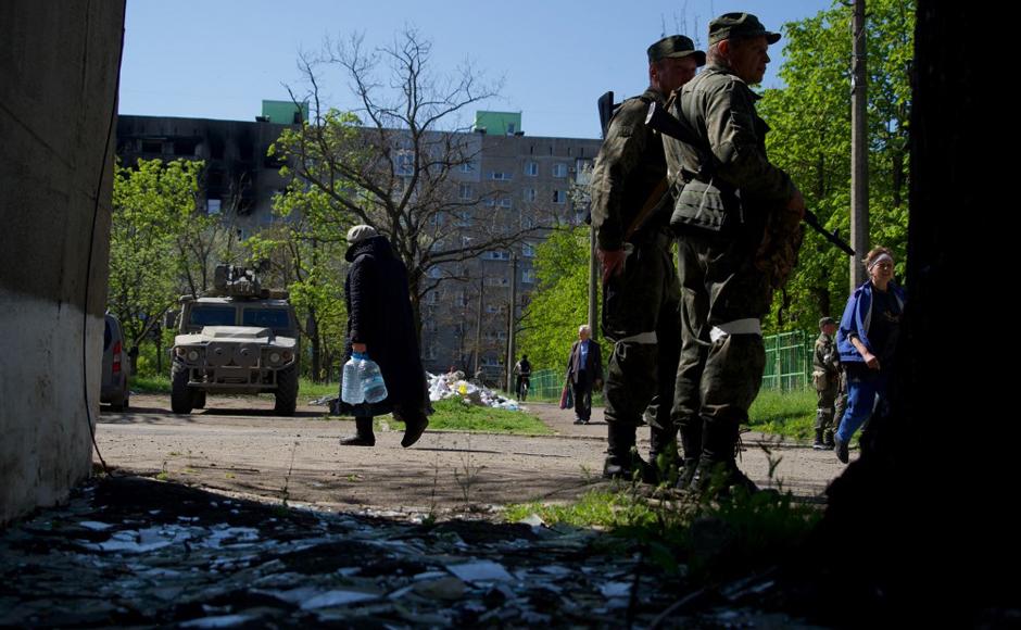 Los residentes caminan en la ciudad de Mariupol mientras los autoproclamados soldados de la República Popular de Donetsk (DNR) vigilan un área en medio de la acción militar rusa en curso en Ucrania.