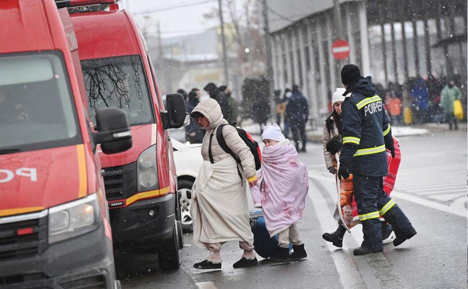 Refugiados provenientes de Ucrania caminan hacia los autobuses de los servicios de emergencia en la frontera ucraniano-rumana.