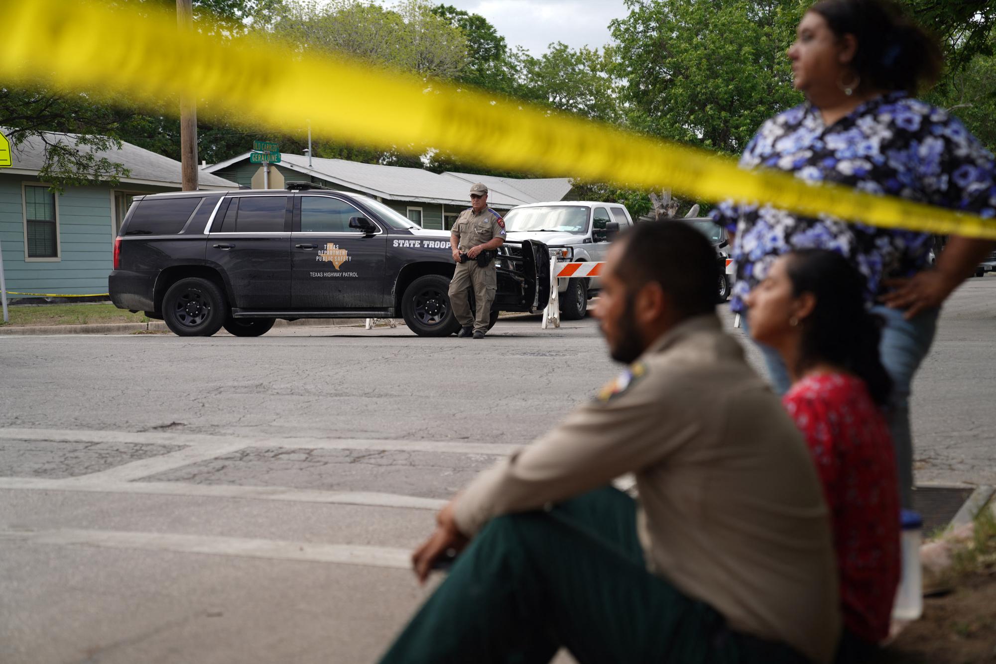 La gente se sienta en la acera afuera de la Escuela Primaria Robb mientras la policía estatal vigila el área en Uvalde, Texas, el 24 de mayo de 2022. - Un hombre armado de 18 años mató a 14 niños y a un maestro en una escuela primaria en Texas el martes. (Foto de allison cena / AFP)