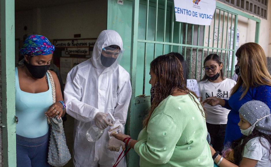 Un funcionario electoral con traje de protección de bioseguridad rocía desinfectante en las manos de un votante a la entrada de un colegio electoral.